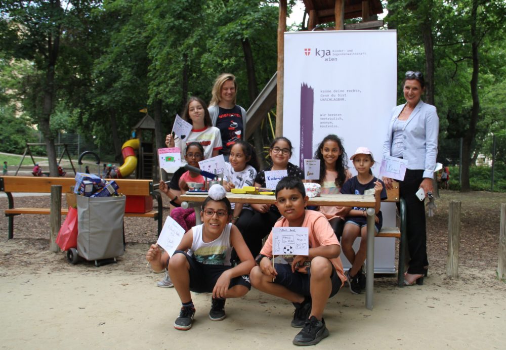 Gruppenfoto: viele Kinder und die Kinder- und Jugendanwältin vor einem Bannder der Kinder- und Jugendanwaltschaft Wien