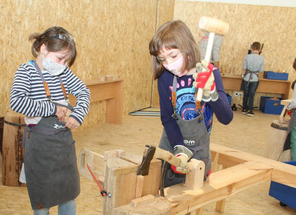 Kinder hacken mit - gesicherter Hacke - und Hammer ein Stück Holz ab