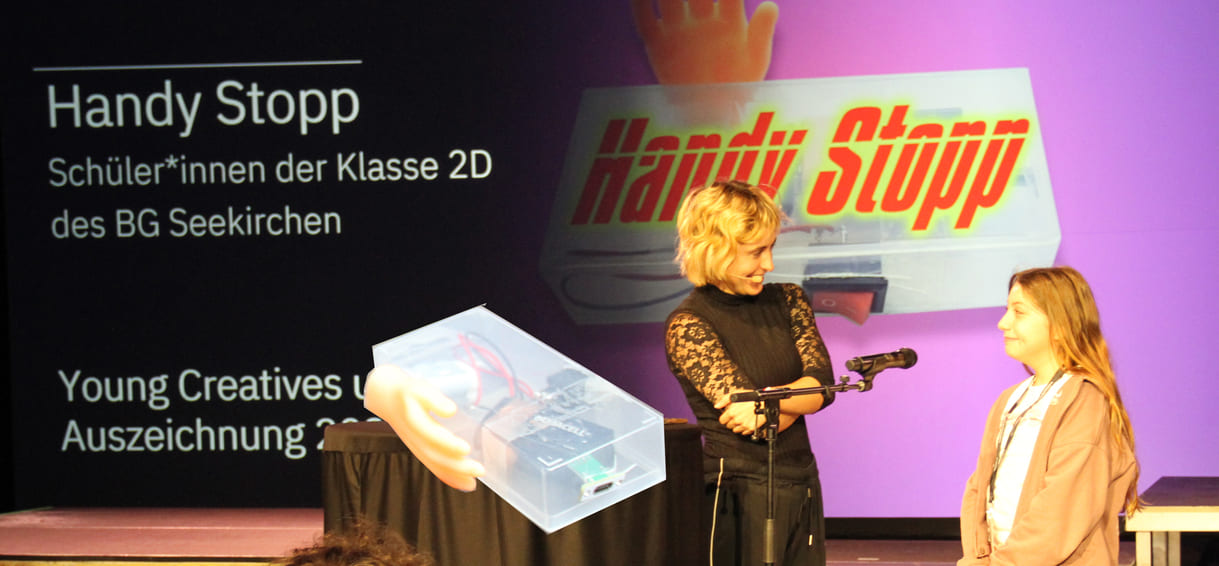 Bildmontage aus einem Foto der Auszeichnung für eine Vertreterin der Salzburger AHS-Klasse, die ein selbst-ironisches Video "Handy Stopp" gedreht und einem Foto des Gerätes, das sie dazu gebaut haben