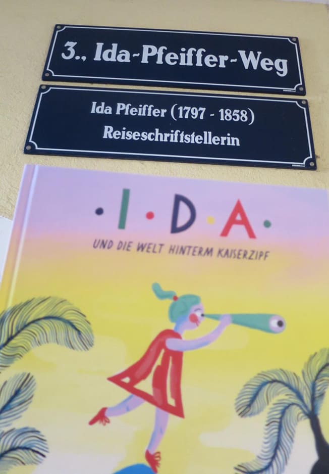 Das Bilderbuch über Ida Pfeffier und Straßenschilder eines Kürzest-Wegs, der nach der Reiseschriftstellerin benannt ist