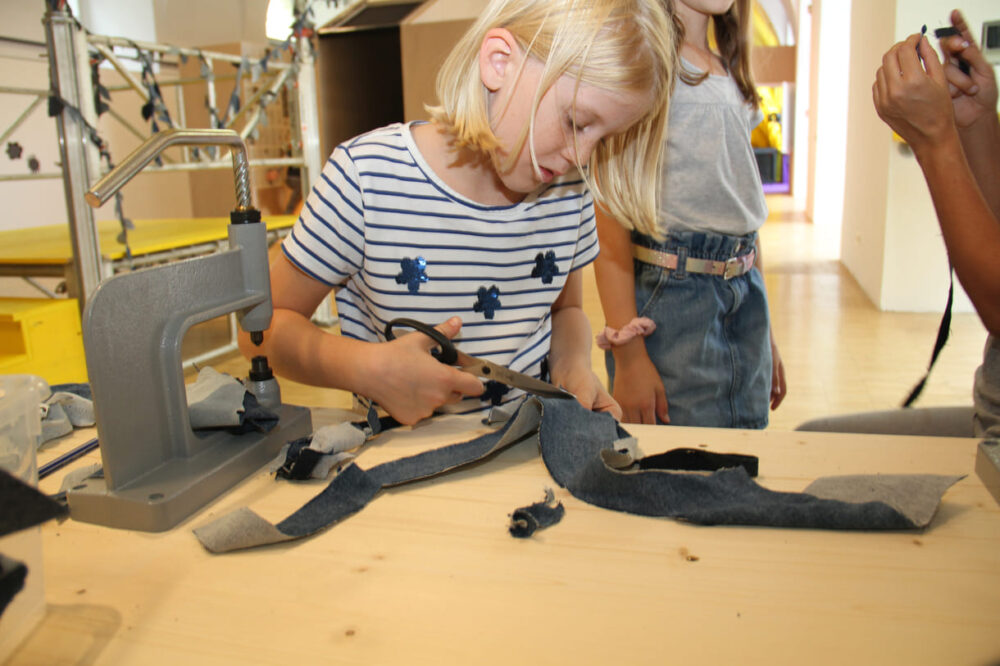 Kinder schneidern aus alten Jeans-Stoffen Blätter für einen blauen Lianen-Dschungel