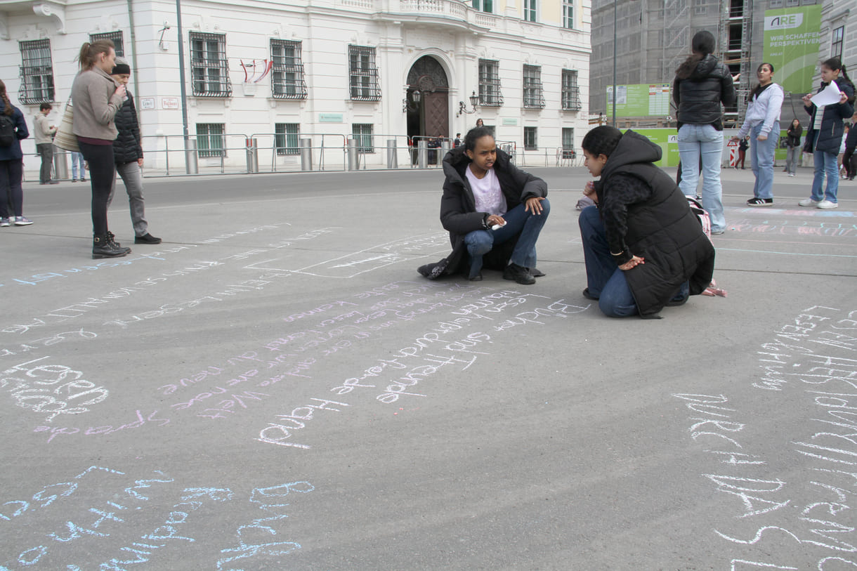 Jugendliche malen mit Kreide Sprüche auf den Boden