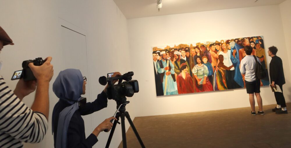 TV-Kamerafrau filmt Besucher:innen und Bilder der Ausstellung