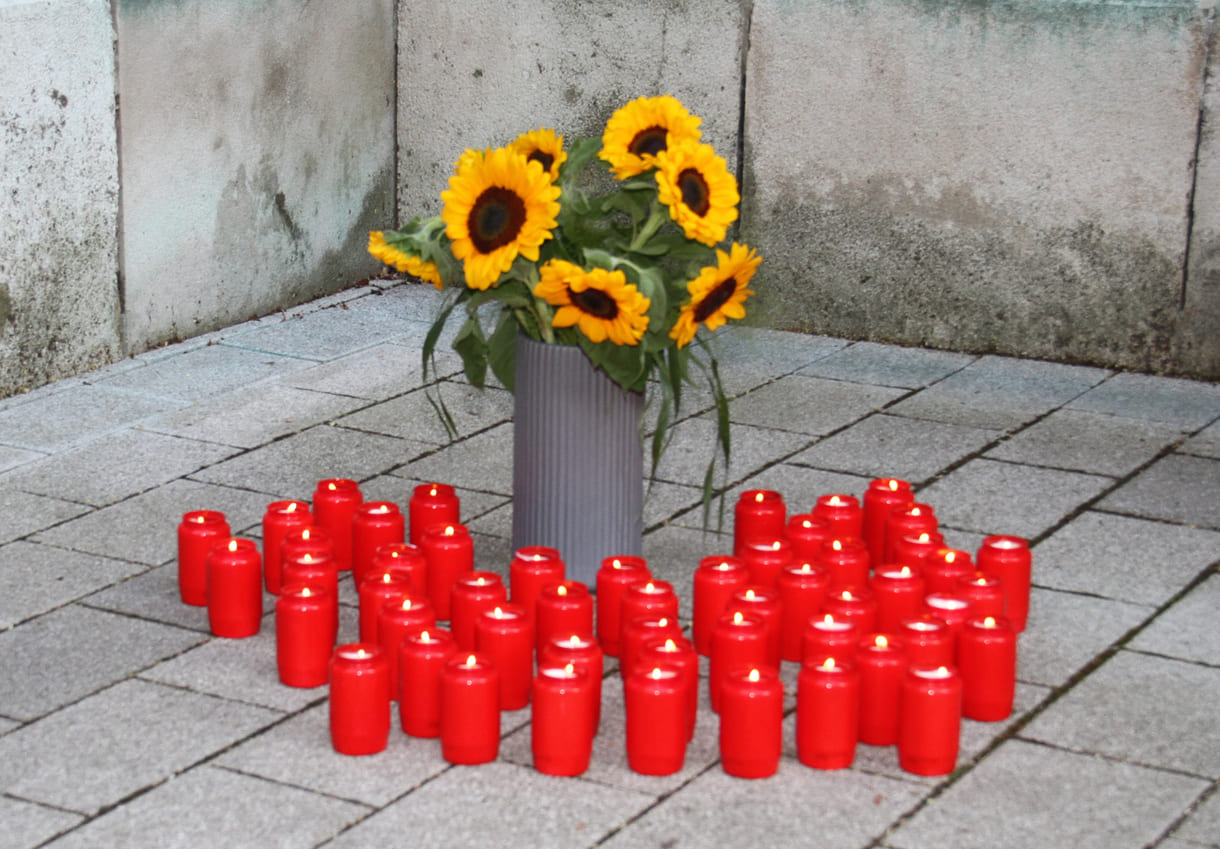 Gedenkkerzen rund um einen Strauß Sonnenblumen, Blume der Rom:nja wie Ceija Stojka in einem Gedicht schrieb