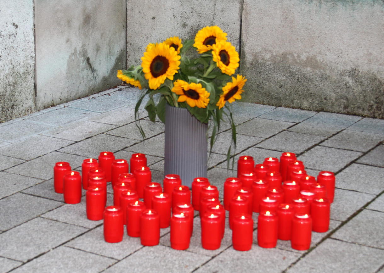 Gedenkkerzen rund um einen Strauß Sonnenblumen, Blume der Rom:nja wie Ceija Stojka in einem Gedicht schrieb