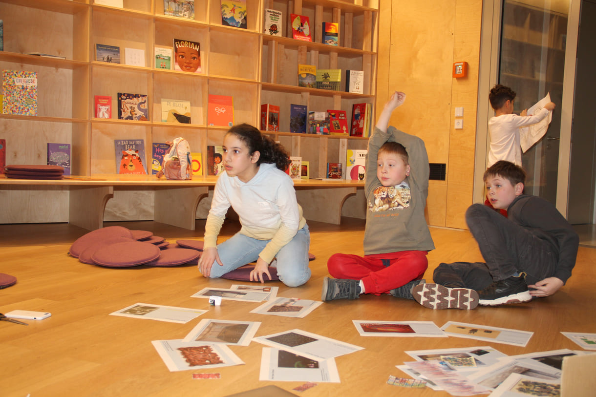 Kinder in der Runde der Ideengeber:innen - mit Bildern und Fotos von Objekten der künftigen Gemeinschaftsausstellung