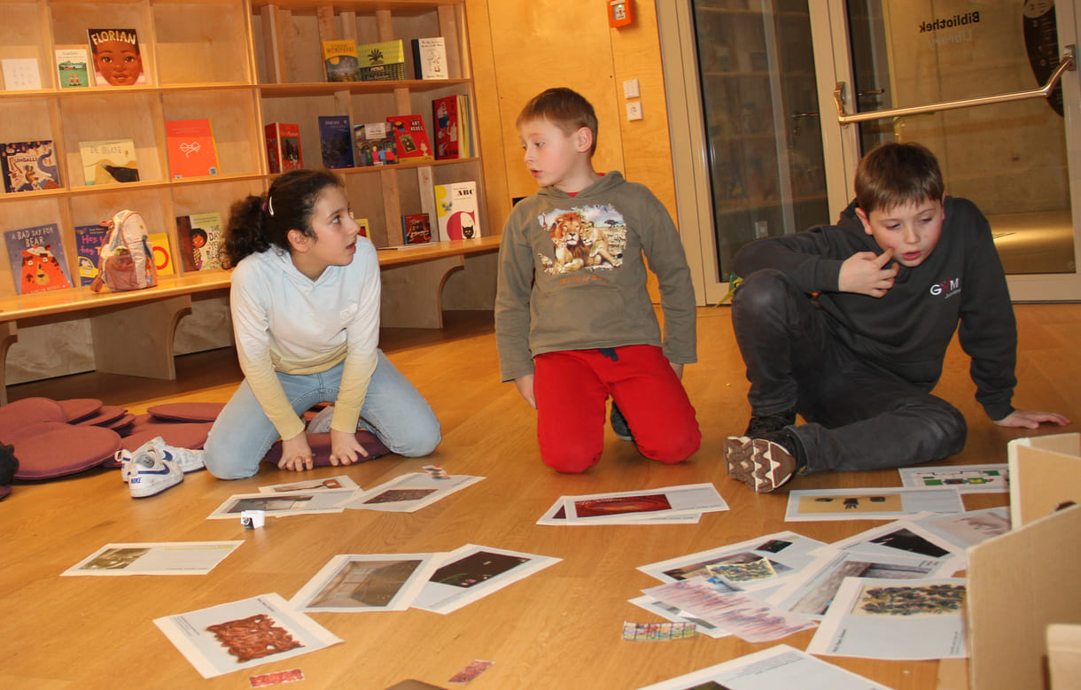 Kinder in der Runde der Ideengeber:innen - mit Bildern und Fotos von Objekten der künftigen Gemeinschaftsausstellung