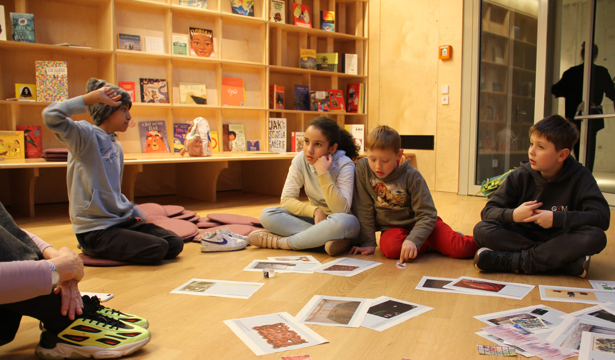 Kinder in der Runde der Ideengeber:innen - mit Bildern und Fotos von Objekten der künftigen Gemeinschaftsausstellung