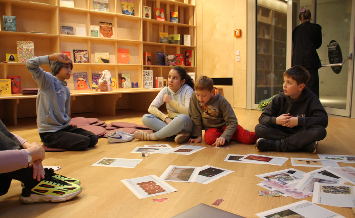 Kinder in der Runde der Ideengeber:innen - mit Bildern und Fotos von Objekten der künftigen Gemeinschaftsausstellung