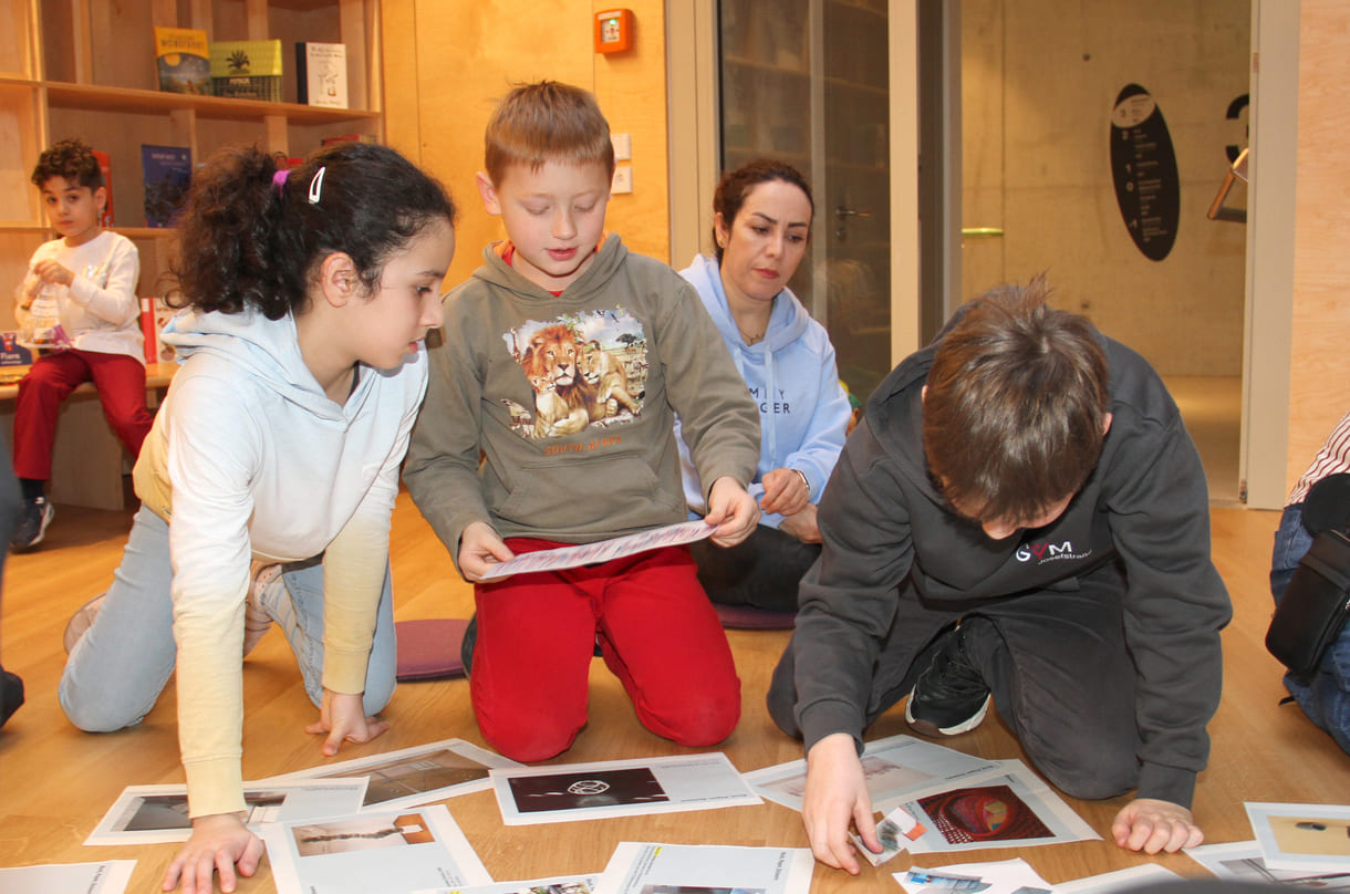 Kinder in der Runde der Ideengeber:innen - mit Bildern und Fotos von Objekten der künftigen Gemeinschaftsausstellung