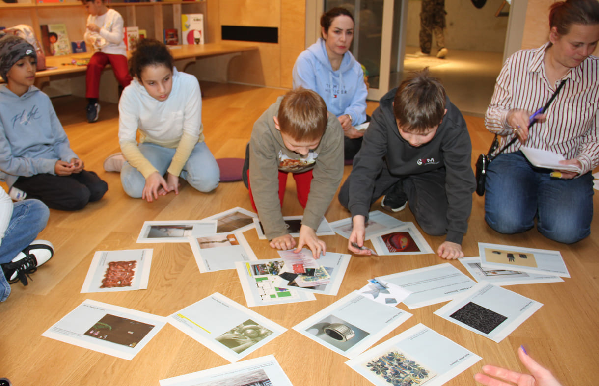 Kinder in der Runde der Ideengeber:innen - mit Bildern und Fotos von Objekten der künftigen Gemeinschaftsausstellung