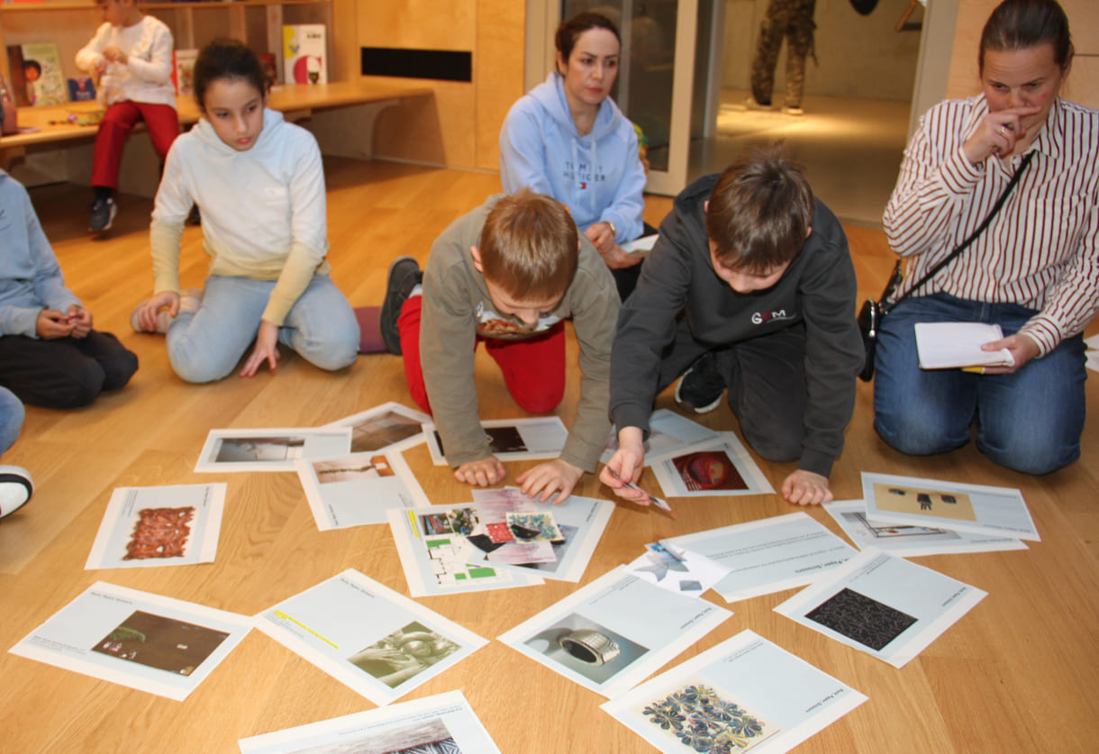 Kinder in der Runde der Ideengeber:innen - mit Bildern und Fotos von Objekten der künftigen Gemeinschaftsausstellung