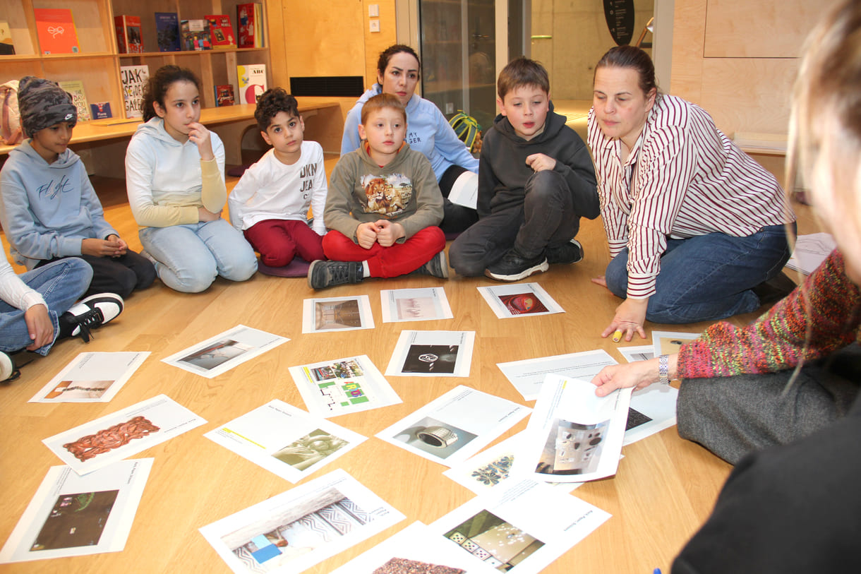 Kinder in der Runde der Ideengeber:innen - mit Bildern und Fotos von Objekten der künftigen Gemeinschaftsausstellung