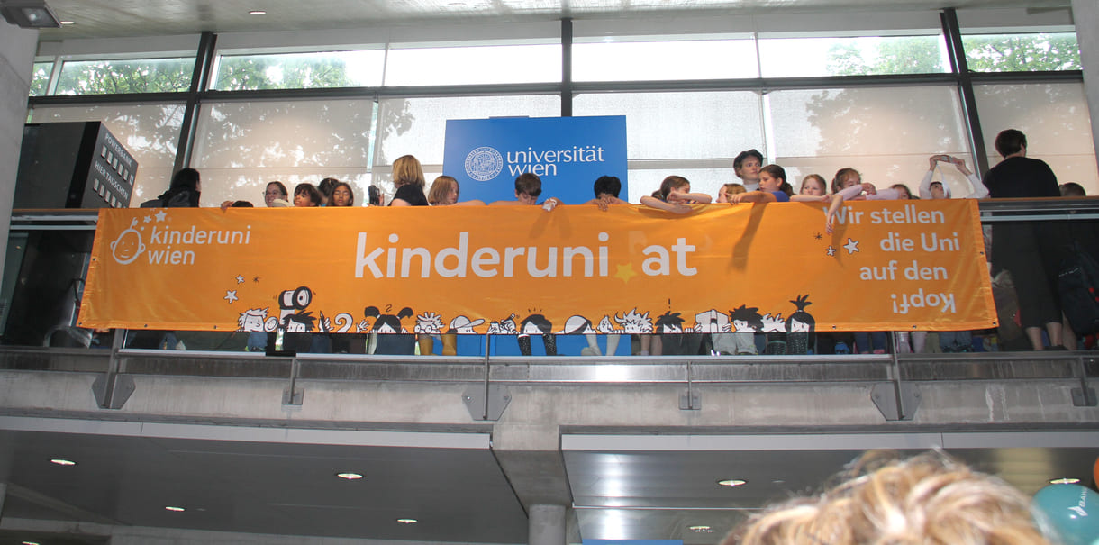 Kinder hinterm - oder vor dem, je nach Sichtweise - Transparent der Kinderuni am Geländer im Hörsaal-Zentrum
