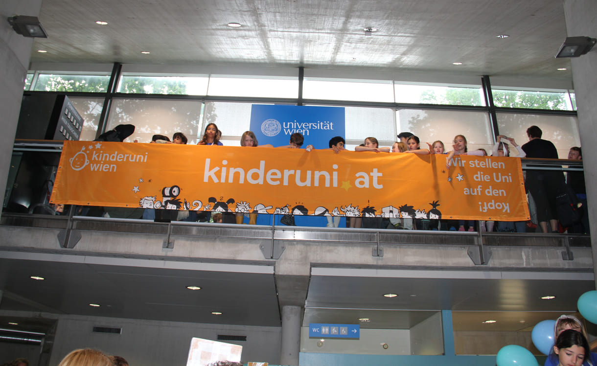 Kinder hinterm - oder vor dem, je nach Sichtweise - Transparent der Kinderuni am Geländer im Hörsaal-Zentrum