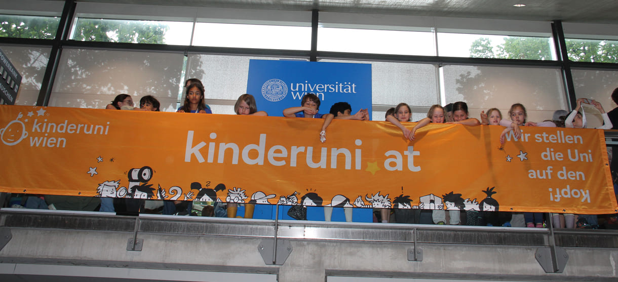 Kinder hinterm - oder vor dem, je nach Sichtweise - Transparent der Kinderuni am Geländer im Hörsaal-Zentrum