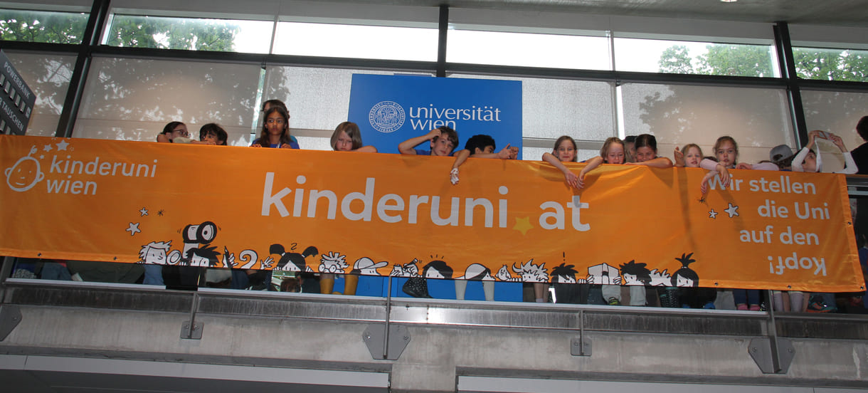 Kinder hinterm - oder vor dem, je nach Sichtweise - Transparent der Kinderuni am Geländer im Hörsaal-Zentrum
