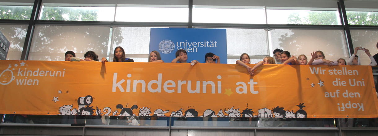 Kinder hinterm - oder vor dem, je nach Sichtweise - Transparent der Kinderuni am Geländer im Hörsaal-Zentrum