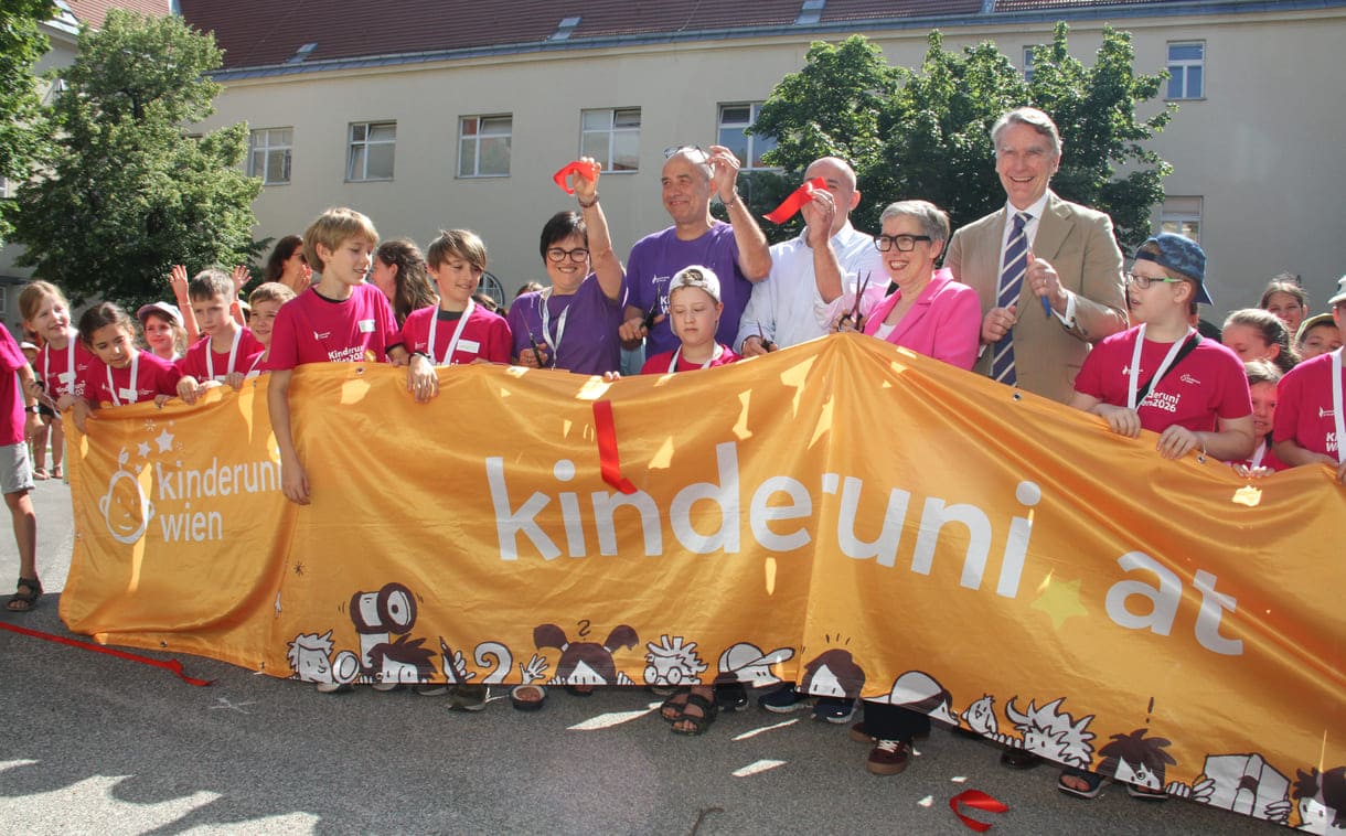 Jung-Studierende und Alt-Lehrende sowie die Organisatorin und der Hauptsponsor mit dem großen Kinderuni Wien-Transparent - und Schnipseln des zerschnittenen roten Bandes