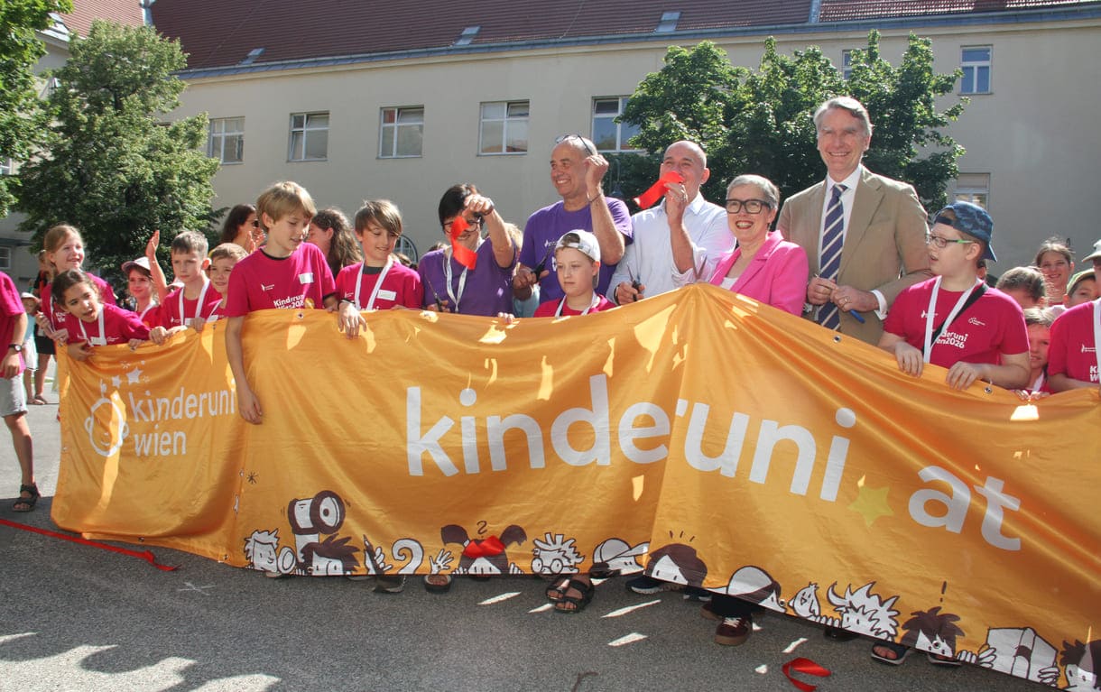 Jung-Studierende und Alt-Lehrende sowie die Organisatorin und der Hauptsponsor mit dem großen Kinderuni Wien-Transparent - und Schnipseln des zerschnittenen roten Bandes
