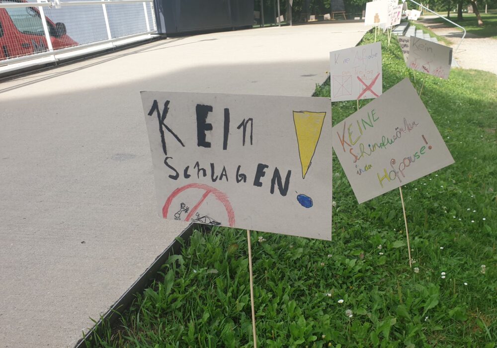 Von Kindern der Volksschule Neuhart geschrieben und gemalte Forderungsplakate auf dem Wiesenstreifen vor dem Grazer Kindermuseum
