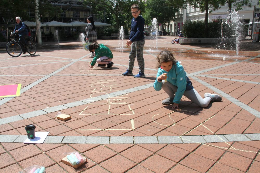 Kinder schreiben mit Straßen-Malkreide systemrelevante Berufe auf den Boden