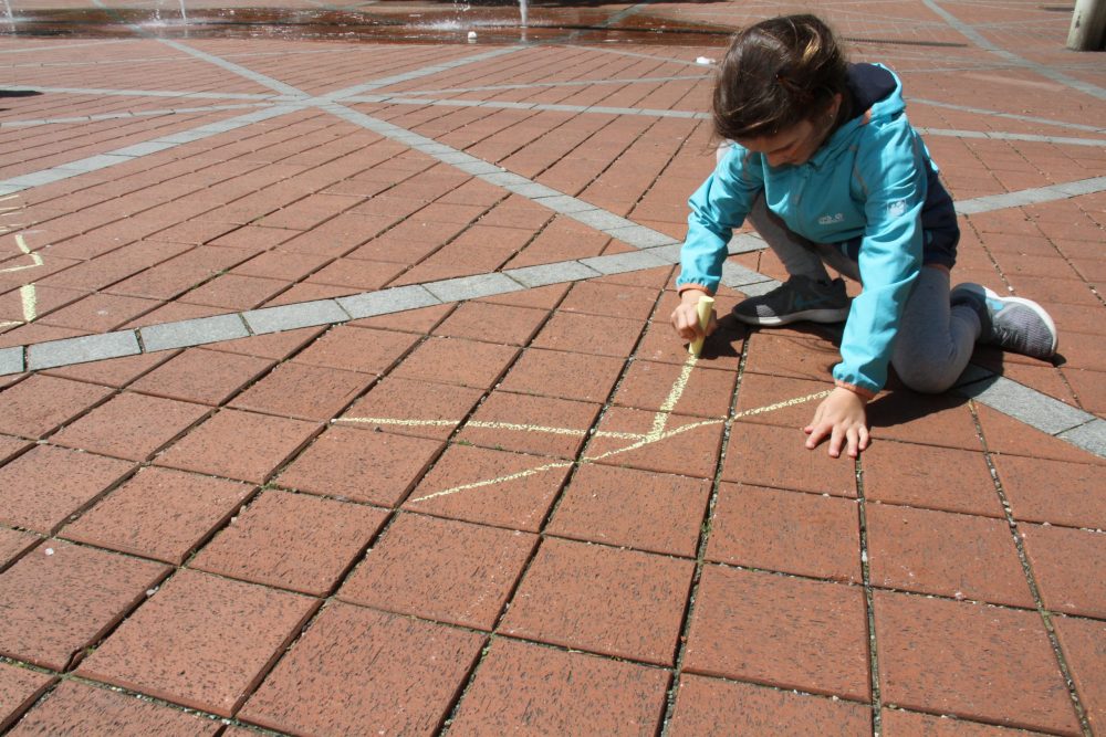Kinder schreiben mit Straßen-Malkreide systemrelevante Berufe auf den Boden