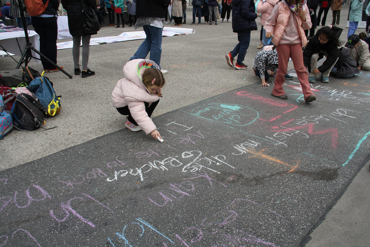 Kinder schreiben Kreidesprüche rund ums Lesen auf den Boden