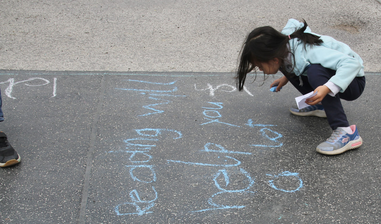 Kinder schreiben Kreidesprüche rund ums Lesen auf den Boden
