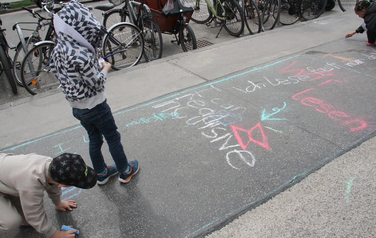 Kinder schreiben Kreidesprüche rund ums Lesen auf den Boden