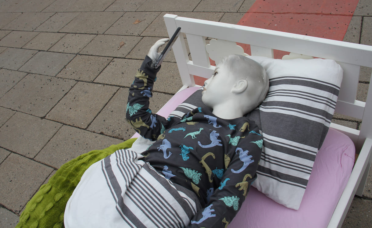 Puppe im Kinderbett starrt aufs Handy - aktionistisch machte der Unicef-Jugendbeirat auf die eigenen Forderungen in Sachen digitaler Kinderschutz aufmerksam