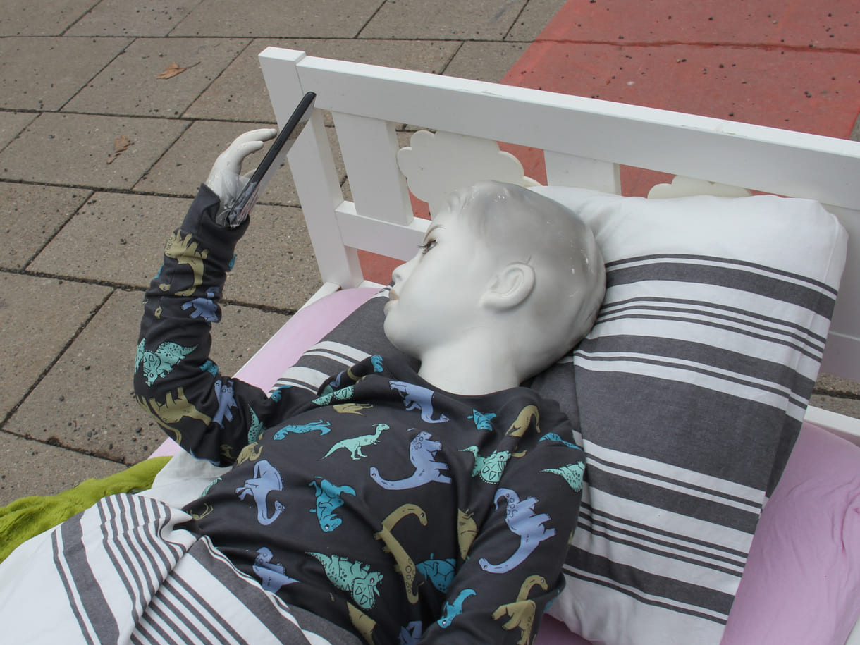 Puppe im Kinderbett starrt aufs Handy - aktionistisch machte der Unicef-Jugendbeirat auf die eigenen Forderungen in Sachen digitaler Kinderschutz aufmerksam