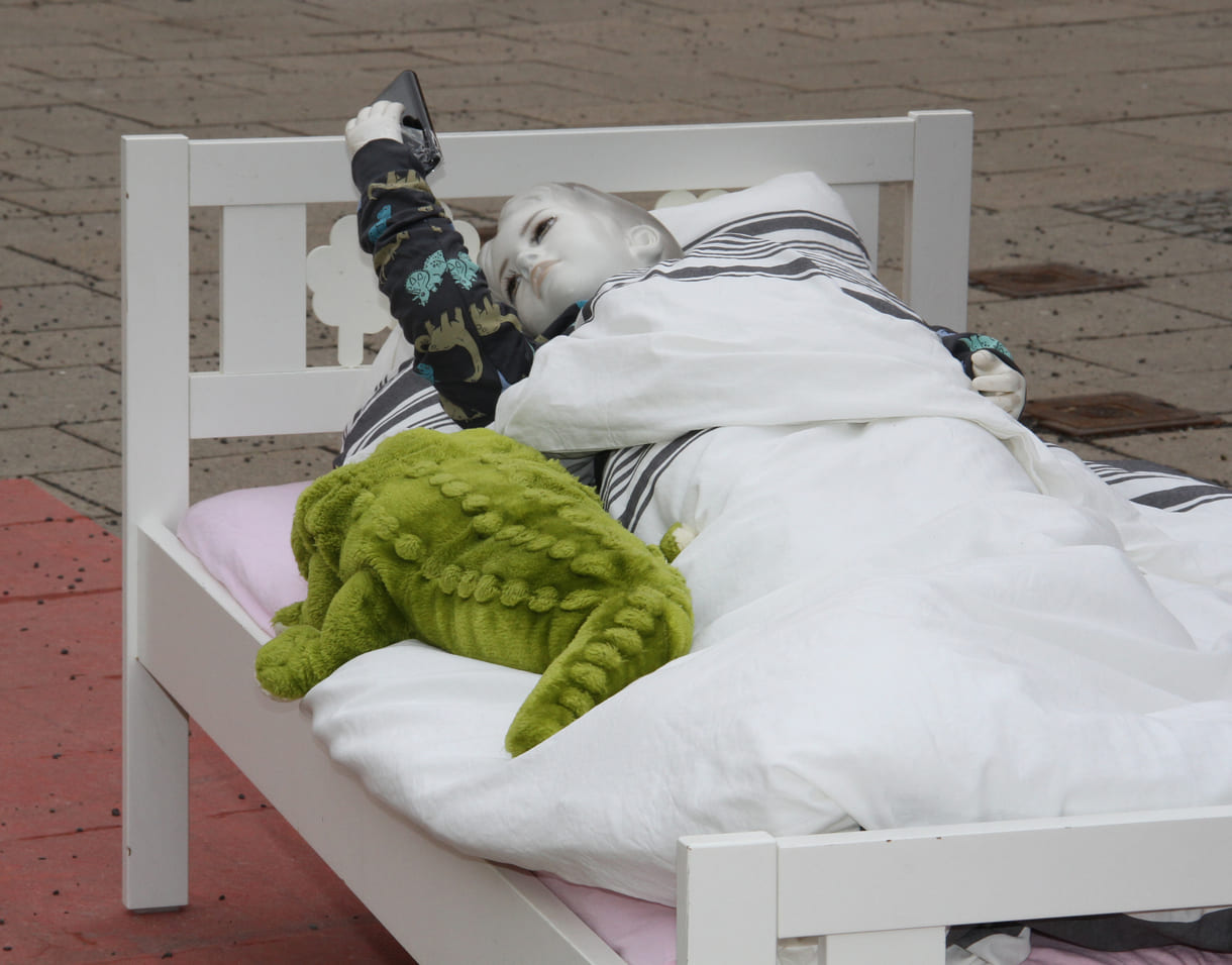 Puppe im Kinderbett starrt aufs Handy - aktionistisch machte der Unicef-Jugendbeirat auf die eigenen Forderungen in Sachen digitaler Kinderschutz aufmerksam