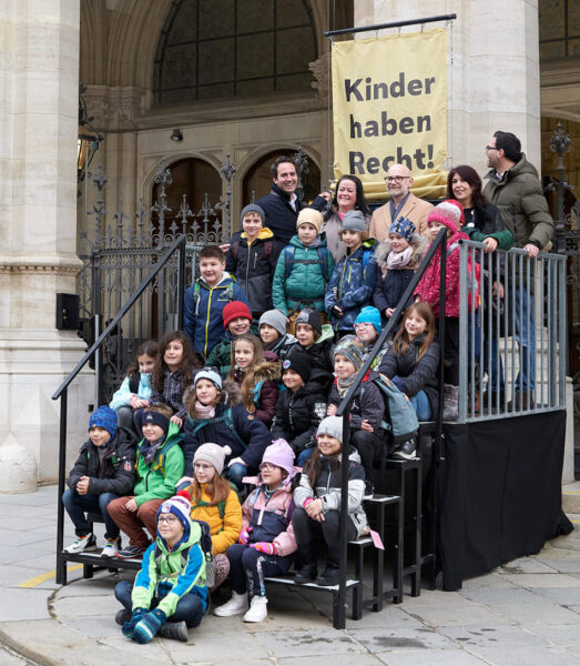 Kinder und Stadtpolitiker:innen hissen am Rathaus Kinderrechtefahnen
