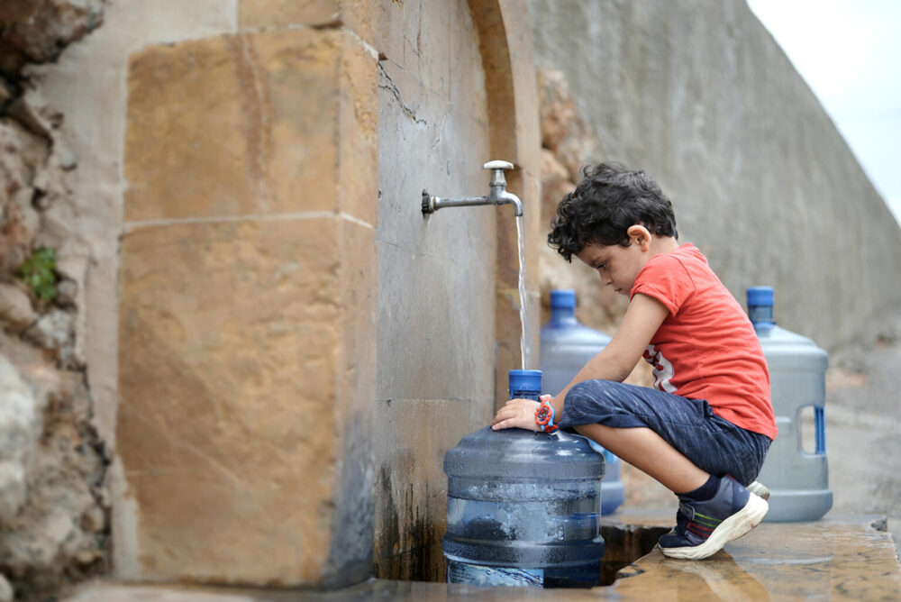Der vierjährige Georgio hilft seinen Eltern, ihre kleinen Wasserbehälter zu füllen, weil sie kein Wasser zu Hause haben.
