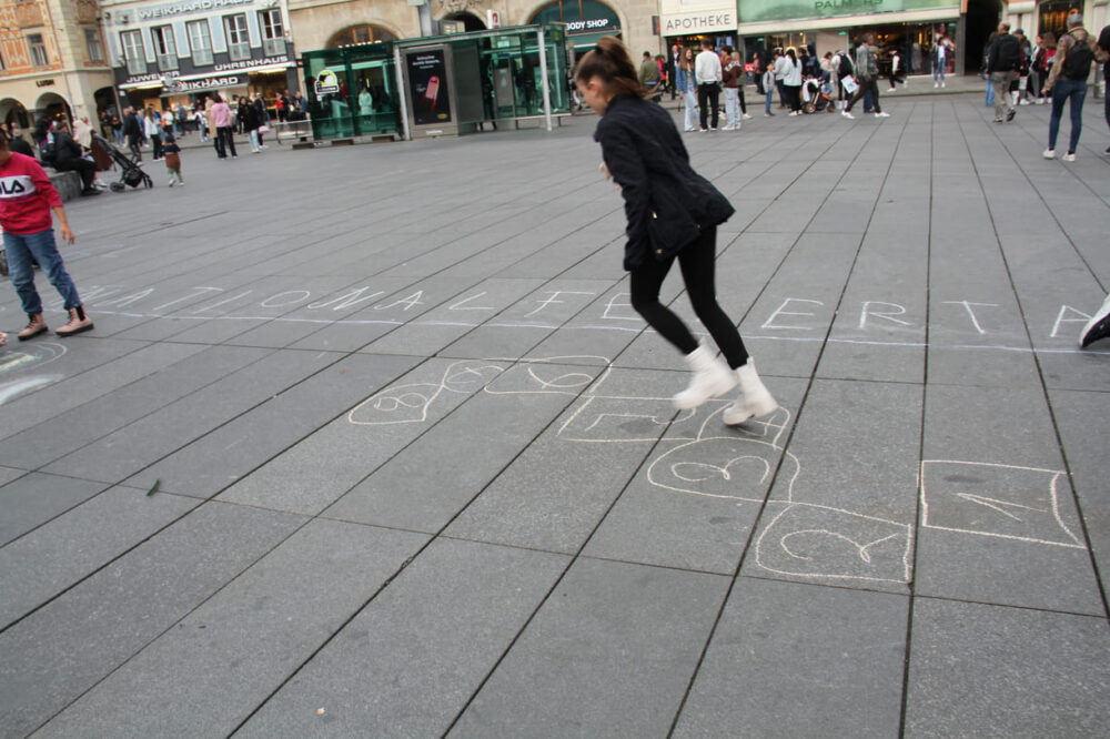Flugs verzieren die Kinder mit Straßenmalkreiden den Platz vor dem Rathaus mit bunten Zeichnungen und Schriften