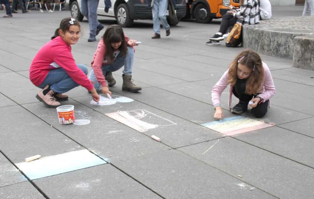 Flugs verzieren die Kinder mit Straßenmalkreiden den Platz vor dem Rathaus mit bunten Zeichnungen und Schriften