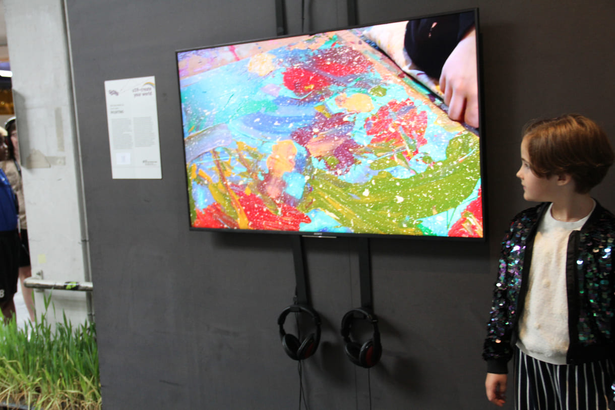U10-Preisträgerin Nea Geršak in der U19-Ausstellung neben dem Screen mit einem Ausschnitt aus dem Video