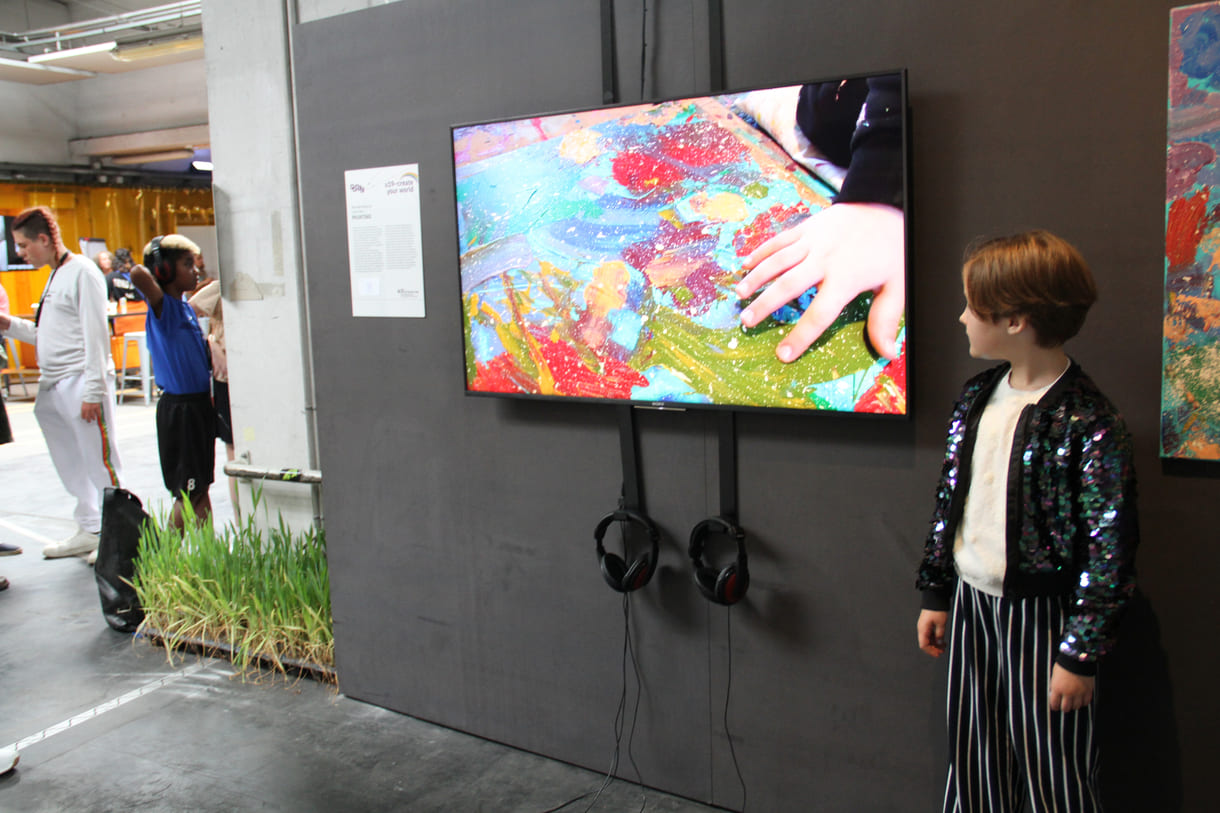 U10-Preisträgerin Nea Geršak in der U19-Ausstellung neben dem Screen mit einem Ausschnitt aus dem Video