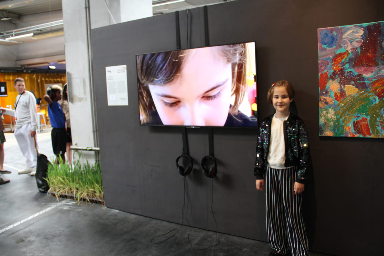 U10-Preisträgerin Nea Geršak in der U19-Ausstellung zwischen Ausschnitt aus dem Video und ihrem gemalten Bild