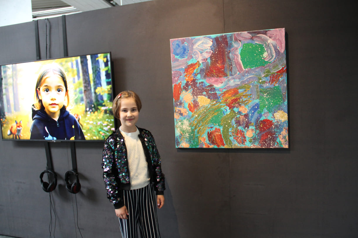 U10-Preisträgerin Nea Geršak in der U19-Ausstellung zwischen Ausschnitt aus dem Video und ihrem gemalten Bild
