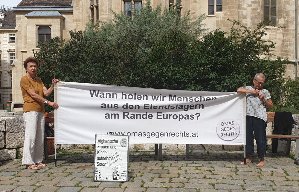 2 Frauen von "Omas gegen Rechts" mit Transparent: "Wann holen wir Menschen aus den Elendslagern am Rande Europas?"