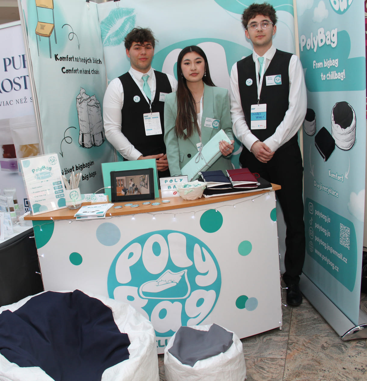 Drei HAK-Schüler:innen aus dem tschechischen Hradec Králové mit - noch nicht gefüllten, aber gefalteten - Sitzsäcken, vor dem Stand zwei mit Polymer-kunststoff gefüllte Lümmelsäcke