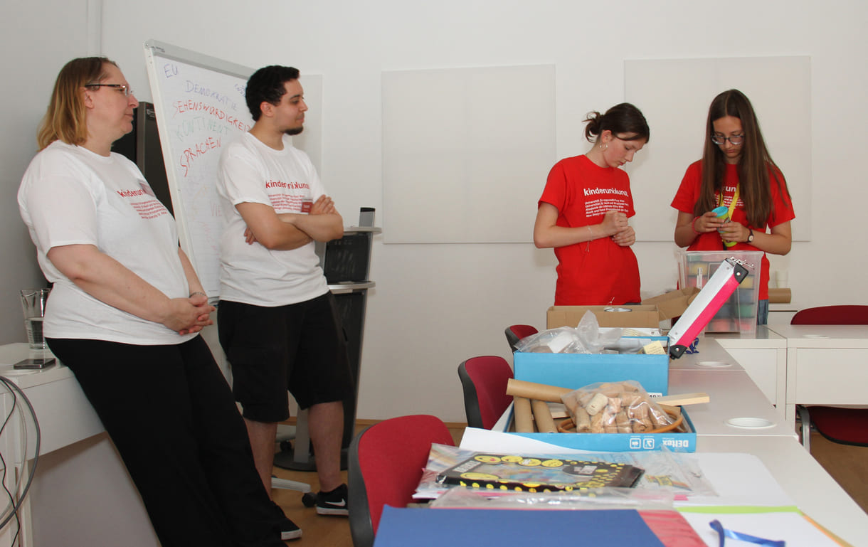 Studierende und Lehrende vor den Tischen mit Materialien