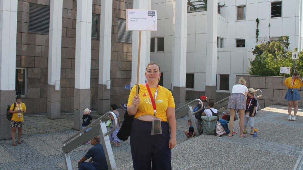 Volunteers in gelben Kinderuni-T-Shirts halten die Schilder mit den Titeln der Lehrveranstaltungen udn begleiten die Jung- und Jüngststudierenden zu ihren Hörsälen