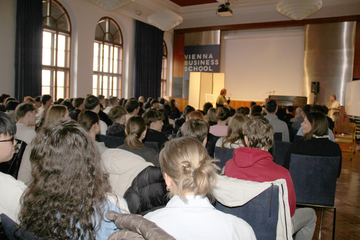 Mit Schüler:innen vollbsetzter Festsaal - ganz vorne, im Bildhintergrund, klein der Schauspieler