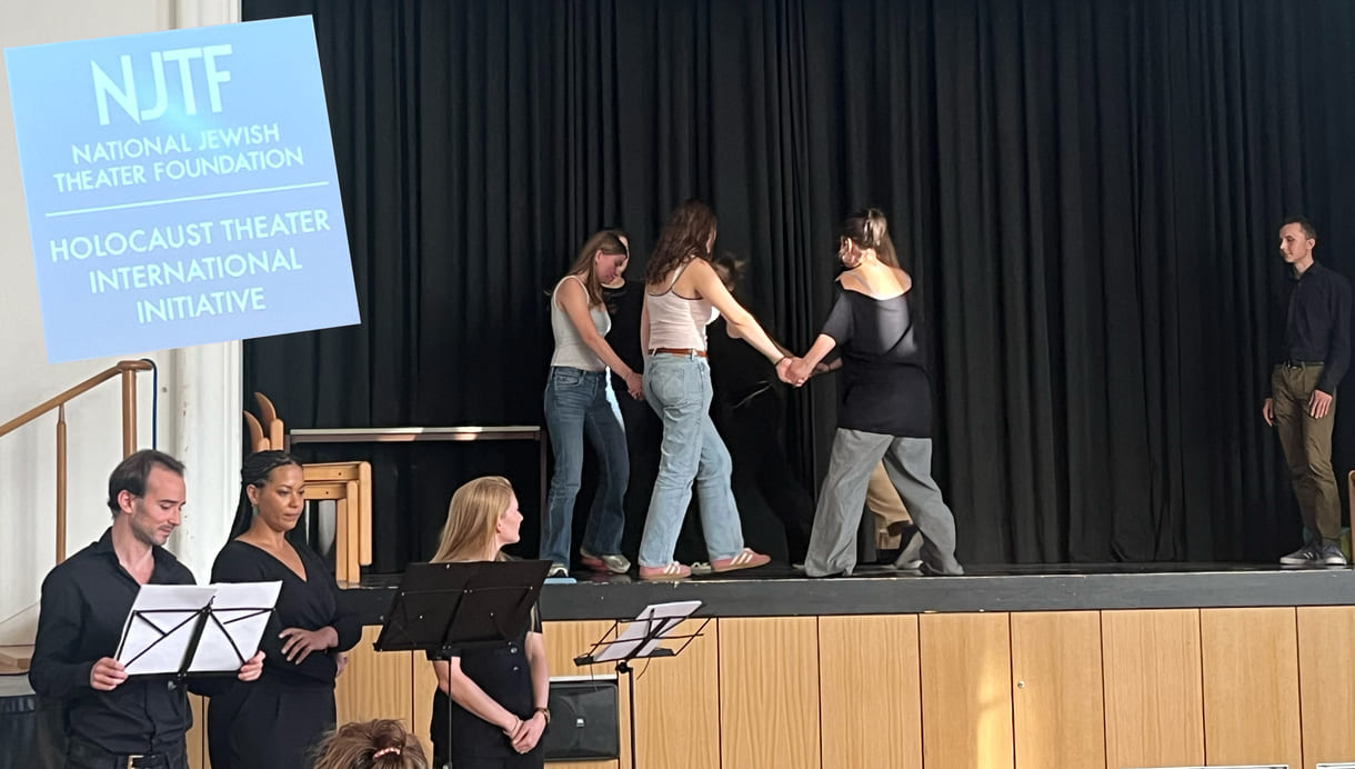 Auf der Bühne spielen Schüler:innen Szenen aus Kindheit und/oder Jugend verfolgter Jüd:innen, davor zitieren Profi-Schauspieler:innen aus den Erinnerungen dreier Verfolgter plus reinmontirtem Logo der internationalen Holocaust-Theater-Initiative der US-amerikanischen Jüdischen Theater Stiftung