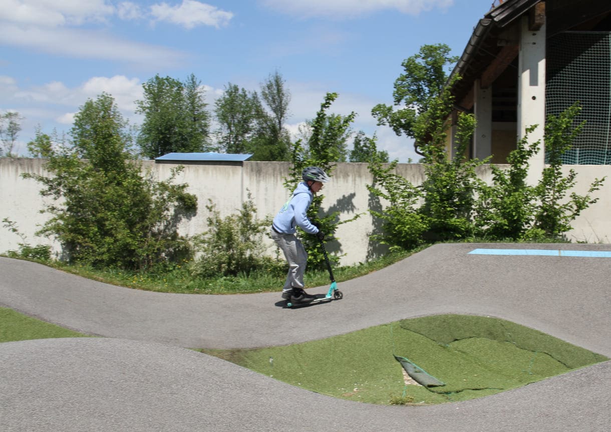 Einer des Radler-Trios düst auch mit einem Scooter über die Pumptrack-Strecke