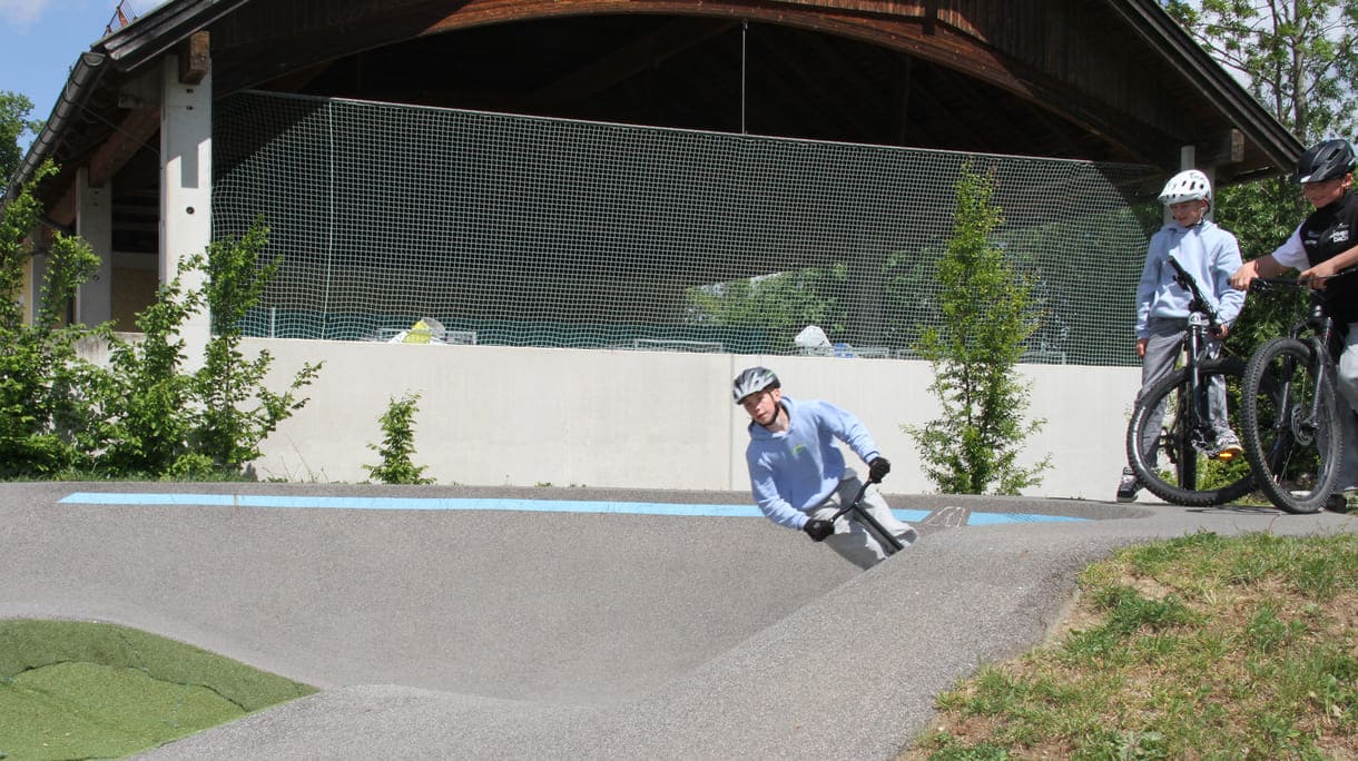 Einer des Radler-Trios düst auch mit einem Scooter über die Pumptrack-Strecke