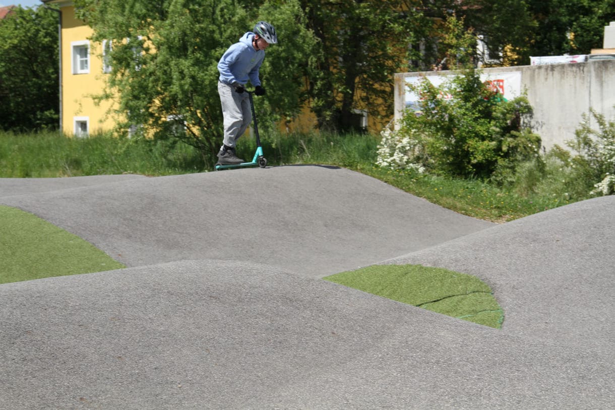 Einer des Radler-Trios düst auch mit einem Scooter über die Pumptrack-Strecke